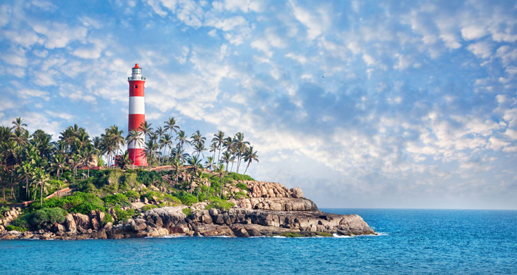 Lighthouse on the rocks near the ocean at blue sky with clouds at Kovalam in the state of Kerala.