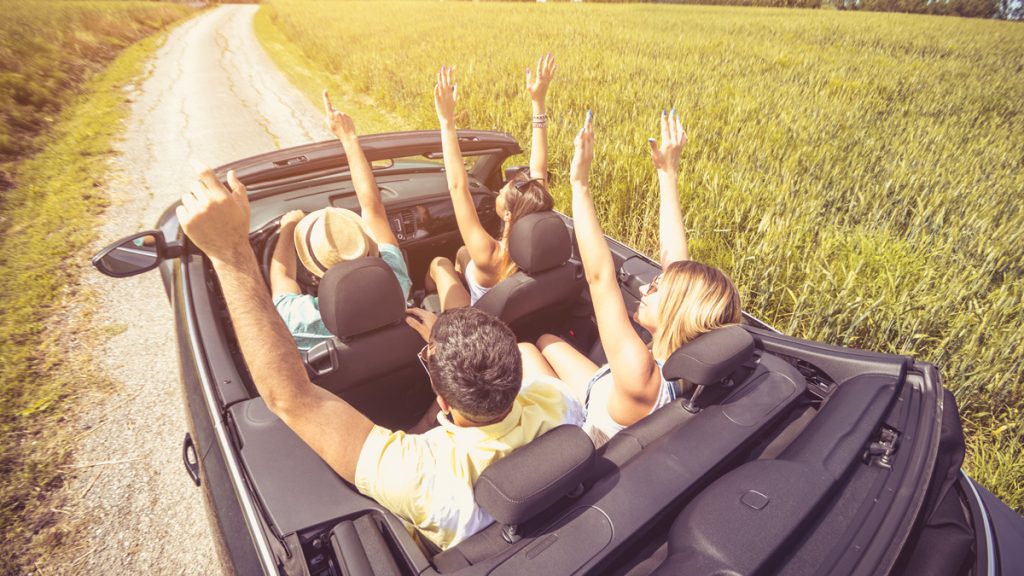 Group of best friends having fun at car trip - Four caucasian people with arms up in a convertible car, view from above