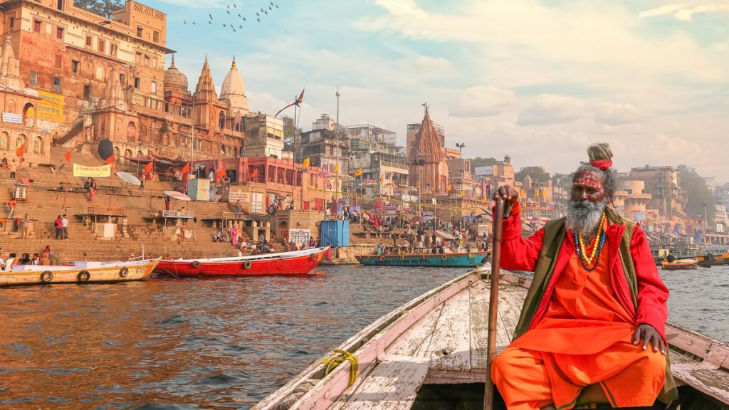 Indian Sadhu baba takes a boat ride on river Ganges overlooking the historic Varanasi city architecture at sunset