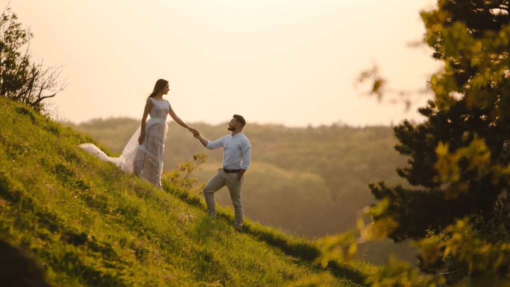 Beautiful young wedding couple of groom and bride standing on the green slope, hill. Sunset in Carpathian mountains